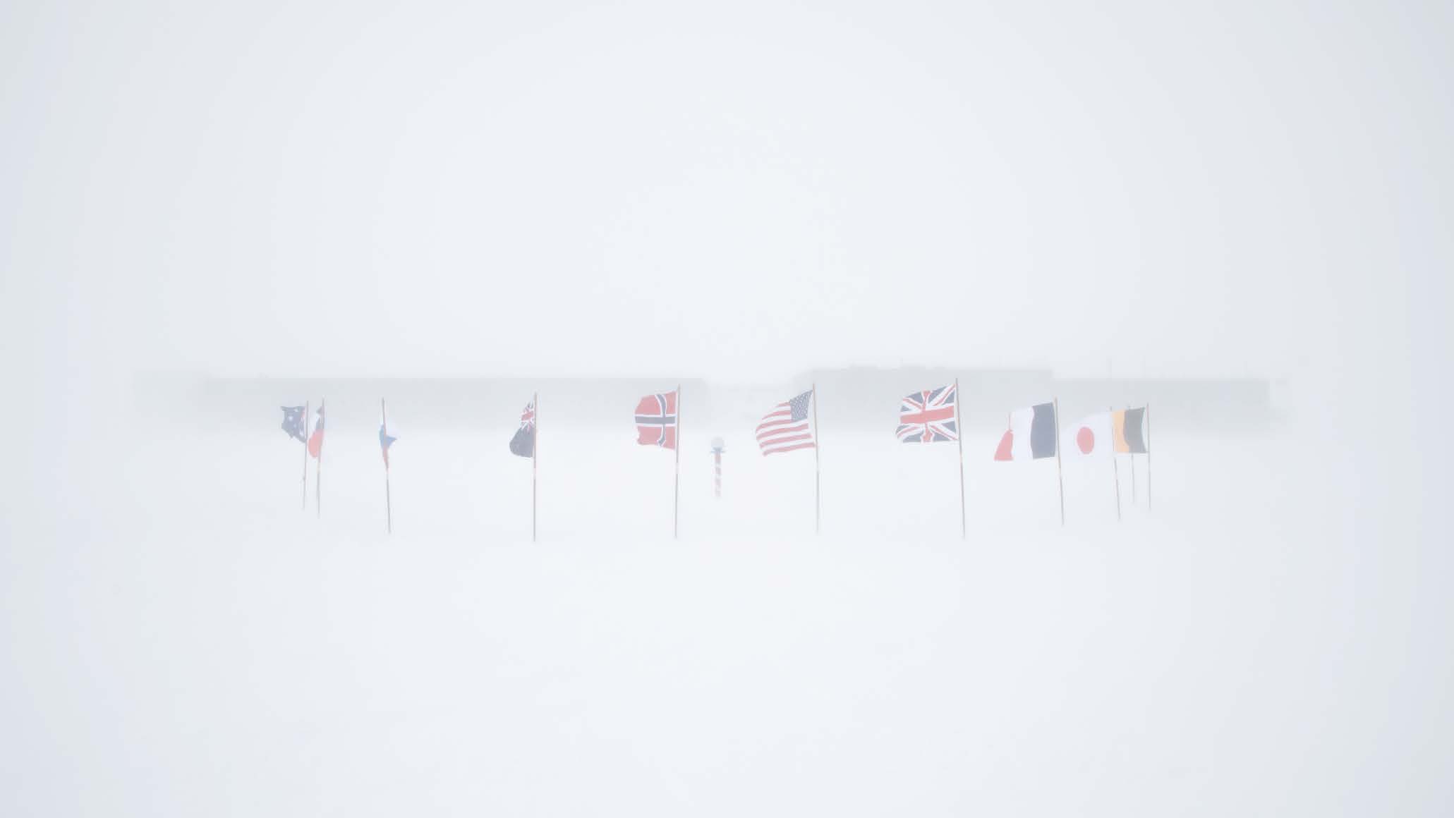 Low visibility, flags billowing with South Pole station blurred in background