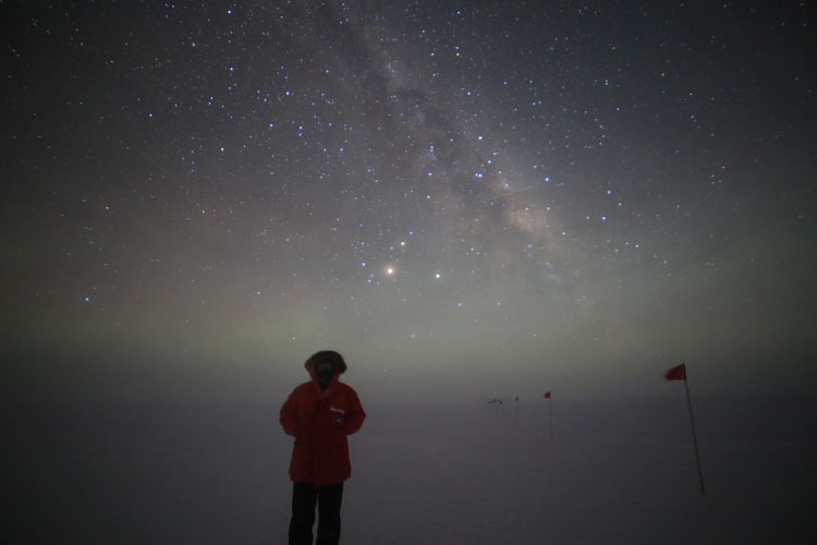 An IceCube winterover standing outside under stars.