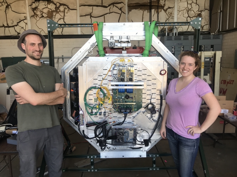<span class="jb-title">Engineer Thomas Meures (left) and PhD student Leslie Taylor (right), both from the University of Wisconsin–Madison, preparing the pSCT camera for installation onto the telescope at the Fred Lawrence Whipple Observatory.&nbsp; The rear of the camera, including electronics for triggering on and recording the 1600 camera pixels at a rate of one billion frames per second, is visible.</span><br/>
